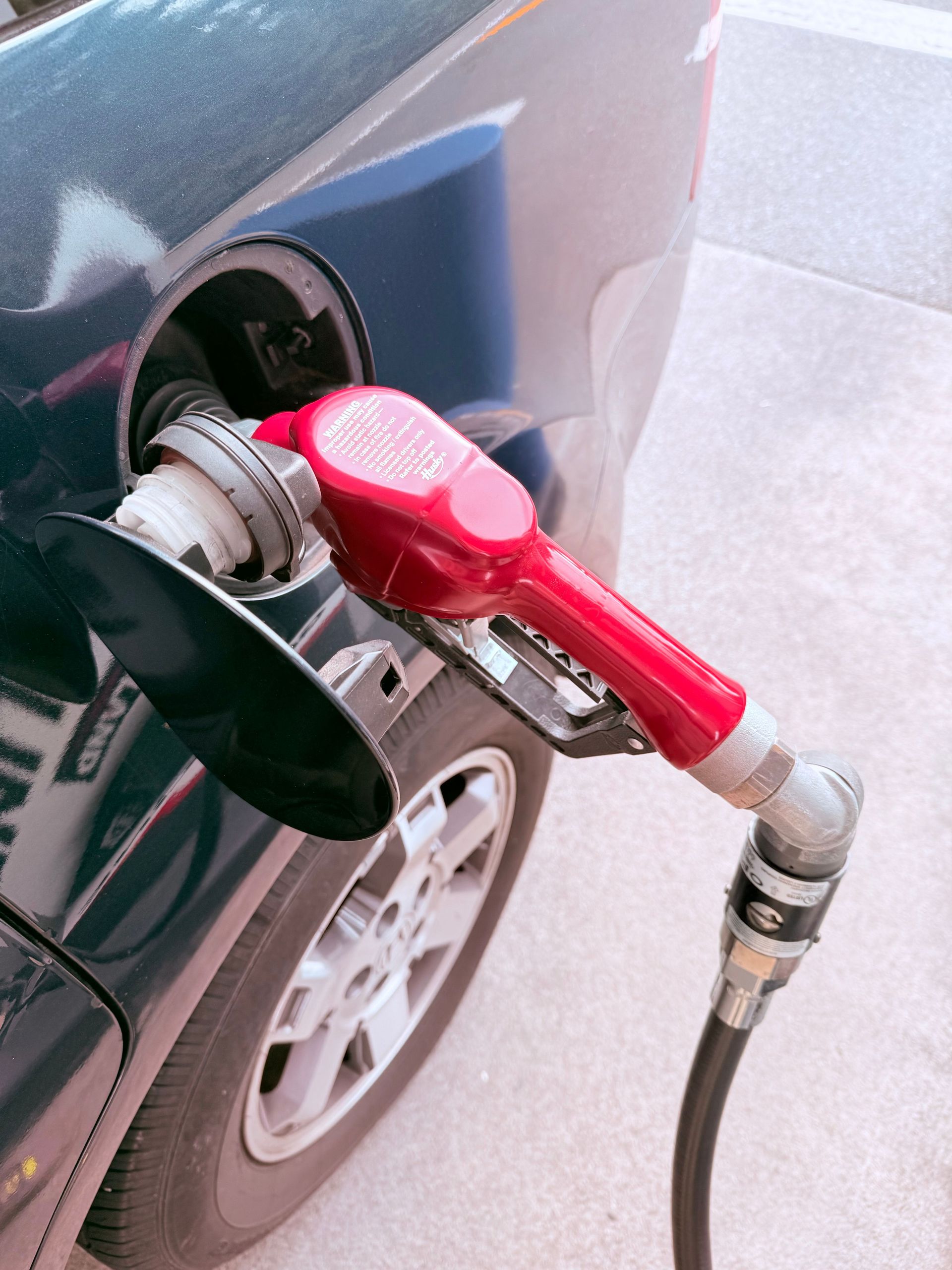 Close-up of a red gas pump fueling a car at a gas station, depicting the refueling process.